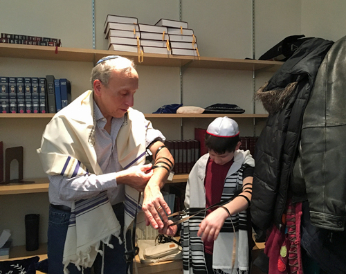 Jeff Bassin shows a student how to wrap the tefillin on his arm.